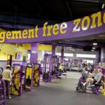Spacious Planet Fitness gym interior with purple and yellow equipment, treadmills, and a large “judgement free” logo on a yellow wall.