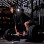 Man performing a bicep curl in a gym while wearing a black tank top, with bold text reading “Muscle and Strength: Best Workout Routines for Maximum Results.